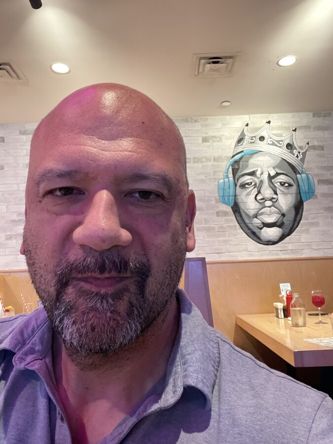 Christopher González in a restaurant, a mural of the Notorious B.I.G. wearing a crown and headphones on the wall behind him