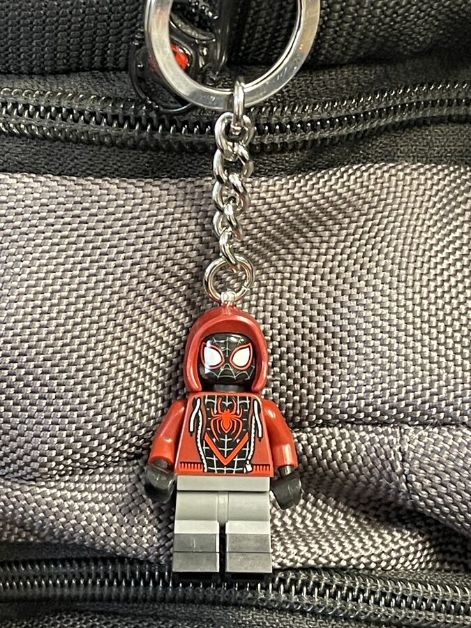 A LEGO Miles Morales minifigure keychain clipped to a backpack